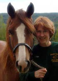 A woman standing next to a horse on top of a hill.